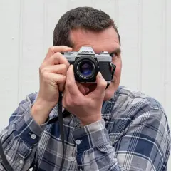 Man med rutig skjorta fotograferar med en Minolta-kamera, en motsats till analog teknik.