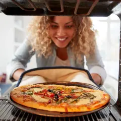 Uśmiechnięta kobieta wyjmuje z piekarnika pyszną pizzę. Widać, na jakim programie piec pizze, bo jest idealnie wypieczona.