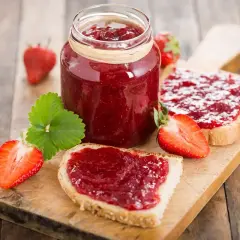 Marmellata di fragole fatta in casa con il Bimby, spalmata su fette di pane fresco, con fragole intere e a metà.