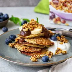 En hög med bananpannkakor toppas med banan, sylt och granola. Ett perfekt bananpannkaka recept för en lyxig frukost eller brunch.