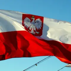 Polska flaga na statku powiewa na wietrze na tle błękitnego nieba. Biało-czerwona flaga z orłem w koronie dumnie reprezentuje kraj.