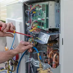 Fachowiec wykonuje serwis pomp ciepła Hitachi, pracując przy otwartej jednostce zewnętrznej z widoczną elektroniką i przewodami.