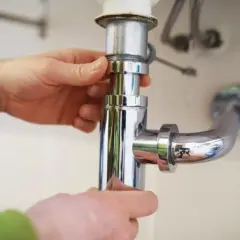 Mains pour démonter un siphon de lavabo, une étape clé pour savoir comment déboucher.
