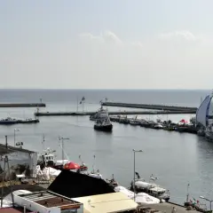 Widok na port Hel z licznymi statkami i łodziami zacumowanymi przy nabrzeżu. W tle widać morze i falochrony.