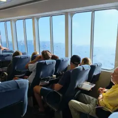 Pasażerowie siedzą w wygodnych fotelach na promie, patrząc przez okna na morze.