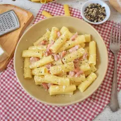 Pyszne pasta alla gricia z guanciale i pecorino, posypana świeżo mielonym pieprzem. Obok ser, tarka i młynek do pieprzu.