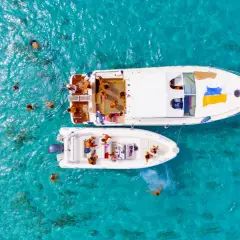 Gente si gode il mare di Favignana, nuotando e rilassandosi su due barche in acque cristalline.