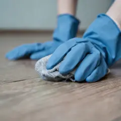 Mani con guanti blu puliscono un pavimento in gres porcellanato opaco con un panno grigio.