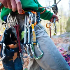 Kletterer mit Ausrüstung für trad climbing, darunter Kletterschuhe und Karabiner, bereit für den Aufstieg.