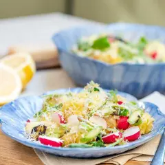 En härlig potatissallad med sparris, rädisor och hyvlad parmesanost. Serveras på en blå tallrik med citroner i bakgrunden.
