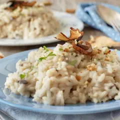 Delicioso risotto de setas cremoso, adornado con trozos de champiñones secos y nueces picadas, servido en un plato azul.