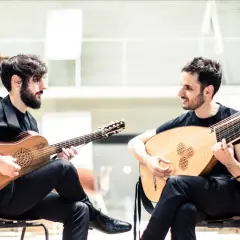 Dos músicos interpretan música renacentista, uno con guitarra barroca y otro con laúd, evocando la obra de Luis de Narváez.