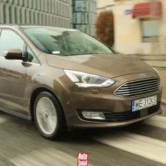 Brązowy Ford Grand C-Max w ruchu miejskim, z widocznymi kroplami deszczu na karoserii i rozmazanym tłem.