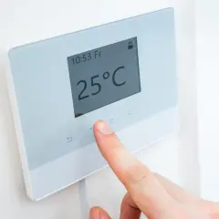 Dedo ajustando uno de los tipos de termostatos para calefacción, mostrando 25°C en pantalla.