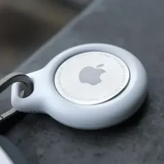 Biały AirTag od Apple, z logo i napisem "Designed by Apple in California". To urządzenie, które pomoże Ci odnaleźć zgubione przedmioty.