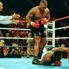 Mike Tyson stands over a fallen opponent, his powerful physique and impressive mike tyson arm length evident. The referee signals the end of the match.