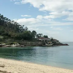 Arena dorada y mar turquesa en la playa de Loira, con casas blancas y una colina boscosa al fondo.