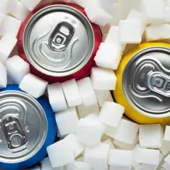 Trzy puszki napojów otoczone kostkami cukru. Czy Mirinda jest zdrowa? Obraz sugeruje, że niekoniecznie.
