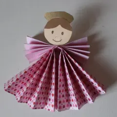 Un adorabile angelo di carta da ritagliare, con un vestito a fantasia di cuoricini rosa e un'aureola dorata.