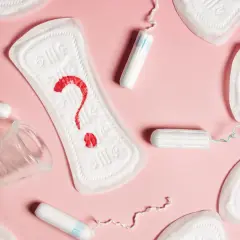 Plamienie 3 dni po okresie? Podpaski, tampony i kubeczek menstruacyjny na różowym tle.
