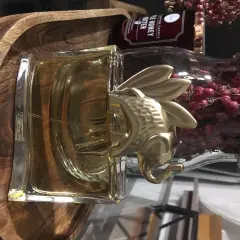 Złoty słoń na flakonie Kenzo Jungle 100ml, otoczony drewnianą misą i różowymi owocami.
