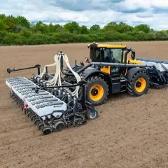 Żółty traktor z przyczepionym nowoczesnym siewnikiem do nawozu ogrodowego pracuje na pustym polu.