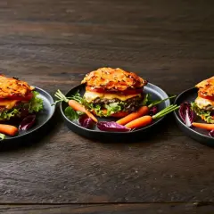 Drei appetitliche Hamburger mit Pommes, garniert mit Karotten und Radicchio auf dunklem Holztisch.