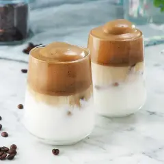 Två glas med krämigt iskaffe, perfekt för ett enkelt iskaffe recept. Kaffebönor sprider sig runt glasen.