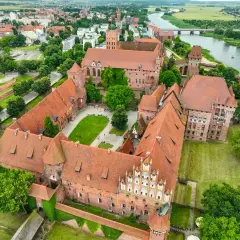 Potężny zamek w Malborku, z czerwonymi dachami i zielonymi dziedzińcami, rozciąga się wzdłuż rzeki Nogat.