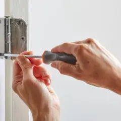 Mains serrant une vis avec un tournevis pour réparer une porte qui grince.