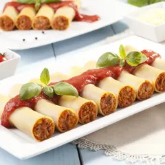 Cannelloni z mięsem i sosem pomidorowym, udekorowane bazylią, na białym talerzu.