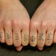 Tatuaż na palcach tworzy napis "UNBROKEN". To jak trwały pierścionek, symbol siły.