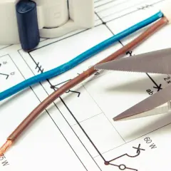 Niebieski i brązowy kabel, gotowe do cięcia, leżą na schemacie elektrycznym.