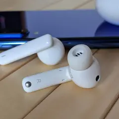 Białe słuchawki Huawei leżą obok niebieskiego smartfona. Dowiedz się, jak podłączyć bezprzewodowe słuchawki Huawei.