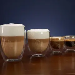 Vier Gläser mit Kaffee und Milchschaum. Das größte Glas zeigt, was ist milchkaffee: geschichtete Milch und Kaffee mit viel Schaum.