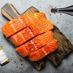 Frischer Lachs auf Holzbrett, daneben Weißwein und Rotwein. Die Frage: welcher Wein zu Lachs? Hier finden Sie die Antwort.