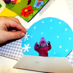 Dziecko tworzy zimowe kreatywne prace plastyczne, dodając płatki śniegu do kuli śnieżnej ze swoim zdjęciem.
