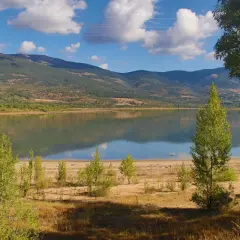 El embalse de Pinilla, con montañas verdes al fondo y un cielo azul con nubes blancas. Reflejos en el agua serena.