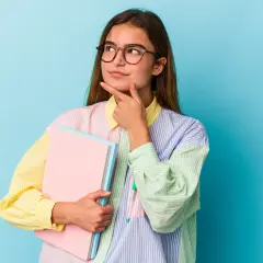 Młoda kobieta w okularach z zeszytami zastanawia się nad ciekawymi kierunkami studiów dla niezdecydowanych.