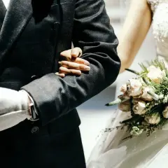 Ojciec prowadzi córkę do ołtarza, trzymając ją pod rękę. Panna młoda w białej sukni z bukietem różowych kwiatów.