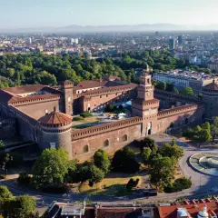 Imponujący zamek Sforzów w Mediolanie, otoczony zielenią i nowoczesnym miastem, z charakterystyczną wieżą zegarową.