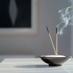 Dos varitas de incienso purificador humean suavemente en un cuenco, creando una atmósfera serena.