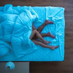 Para nóg pod niebieską kołdrą na łóżku.