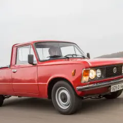 Czerwony fiat 125p pickup w ruchu, z kierowcą za kierownicą. Klasyk na drodze.