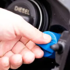 Hand schraubt blauen AdBlue-Deckel ab. Diesel-Tankdeckel daneben.