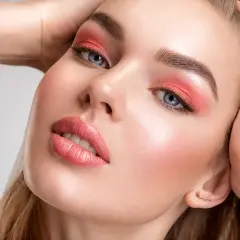 Viso di donna con ombretto corallo e un delicato blush o fard sulle guance.