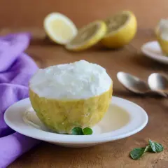 Sorbetto al limone veloce servito in un limone scavato, con limoni affettati e un tovagliolo viola sullo sfondo.