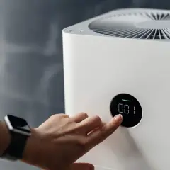 Mano ajustando un climatizador moderno con pantalla digital.