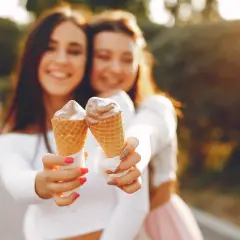 Dwie uśmiechnięte dziewczyny trzymają lody w wafelkach. Czy lody tuczą? Może odrobina przyjemności nie zaszkodzi!