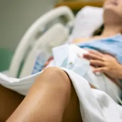 Kobieta w szpitalnym łóżku, przygotowująca się do porodu. Czeka na nią "koktajl położnej", który pomoże jej w tym ważnym momencie.